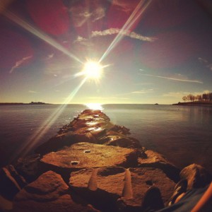 a rock wall with a body of water and the sun shining through