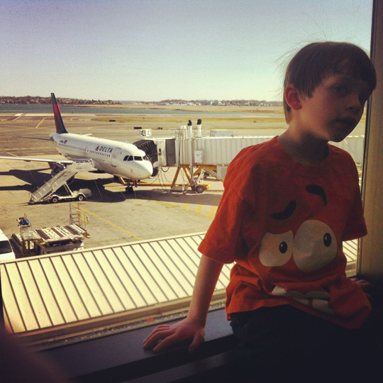 a boy sitting in a window looking out a window at an airplane